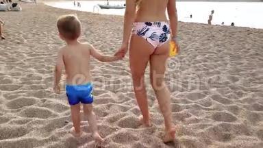 <strong>年轻母亲</strong>手<strong>牵</strong>着孩子在沙滩上散步的4K视频。 幼儿男孩在海滩上与